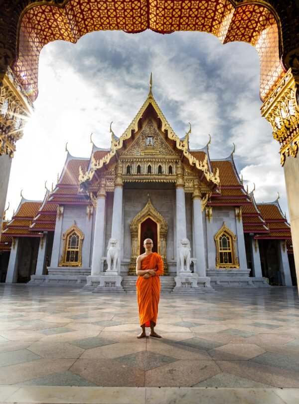 A Buddhist monk standing in front of the iconic Wat Benchamabophit Temple, Bangkok, capturing spiritual tranquility.