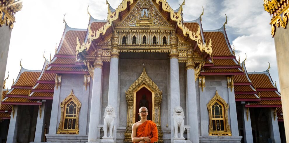 A Buddhist monk standing in front of the iconic Wat Benchamabophit Temple, Bangkok, capturing spiritual tranquility.