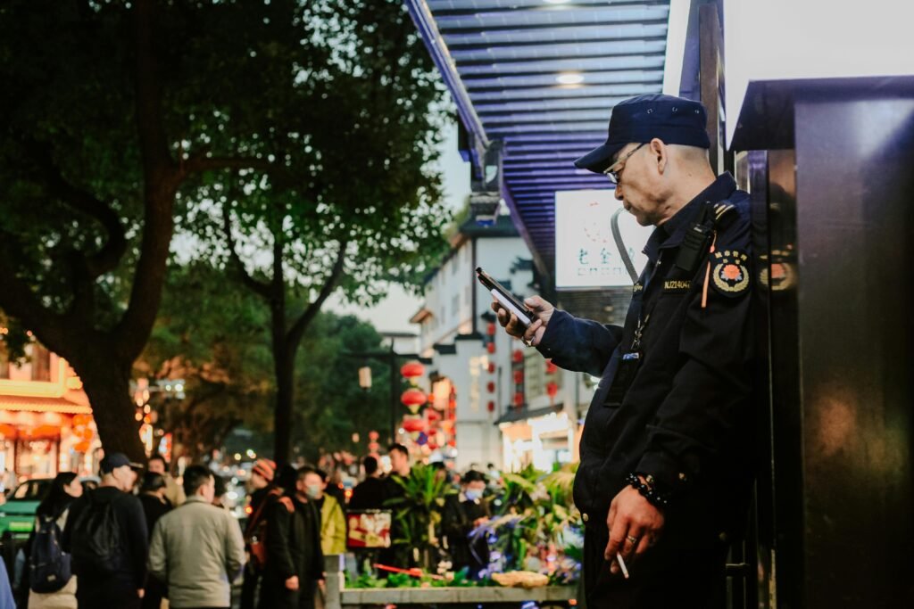 A street guard stands focused on his phone amid the bustling night streets of Nanjing, China.