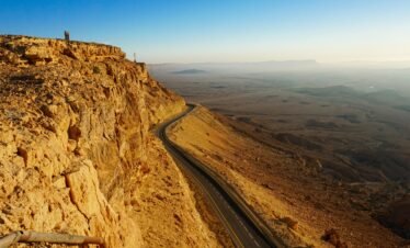 Explore the breathtaking arid landscape of the Mitzpe Ramon Crater with a winding road and expansive desert views.