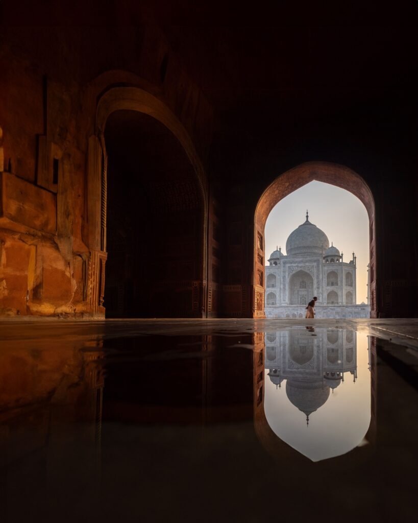 Taj Mahal framed by archway with serene reflection enhances its iconic beauty at dawn.