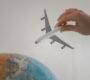 A hand holds a toy airplane above a globe, symbolizing travel and exploration.