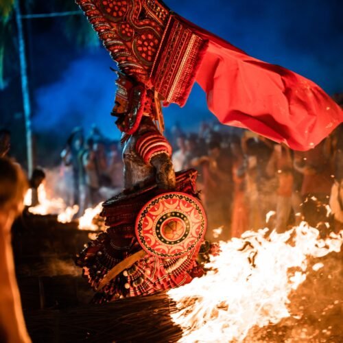 A vivid portrayal of Theyyam ceremony in Udinur, India, amidst fire and vibrant costumes at night.