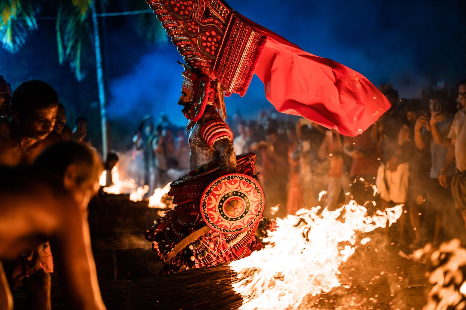 A vivid portrayal of Theyyam ceremony in Udinur, India, amidst fire and vibrant costumes at night.