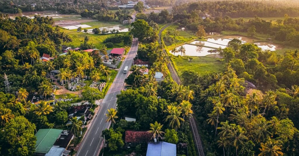 Aerial photograph capturing a lush green countryside with a road and railway at sunset.