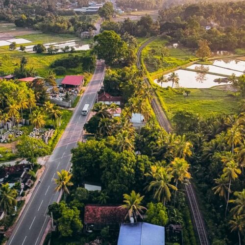 Aerial photograph capturing a lush green countryside with a road and railway at sunset.