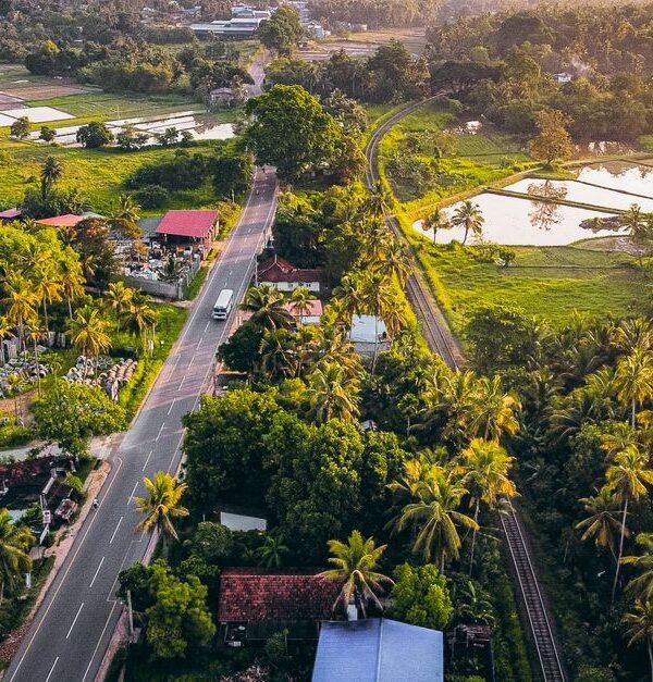 Aerial photograph capturing a lush green countryside with a road and railway at sunset.
