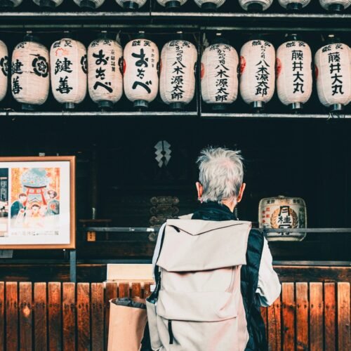 Back view of traveler with backpack looking at hanging Japanese lanterns outdoors.
