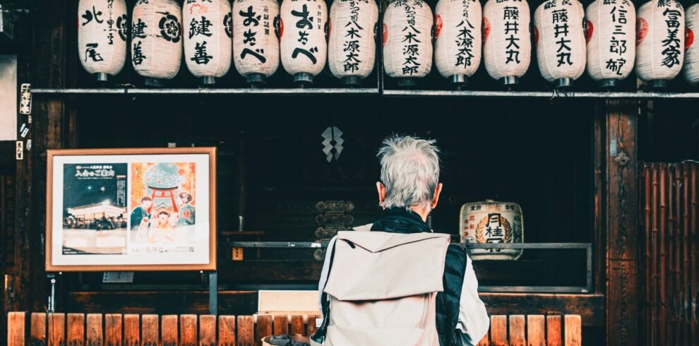 Back view of traveler with backpack looking at hanging Japanese lanterns outdoors.
