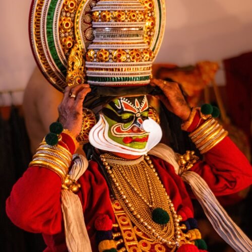 A Kathakali performer donning traditional attire and face makeup backstage, capturing the essence of Indian classical dance.