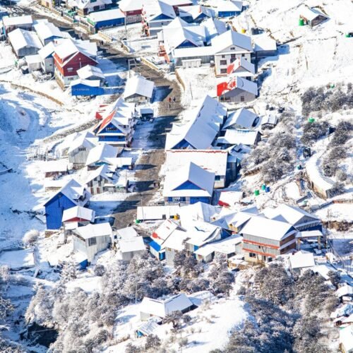 Aerial shot of a snow-covered mountain village with colorful roofs, creating a picturesque winter scene.