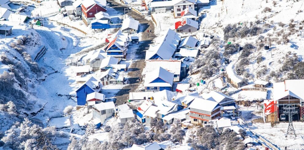Aerial shot of a snow-covered mountain village with colorful roofs, creating a picturesque winter scene.