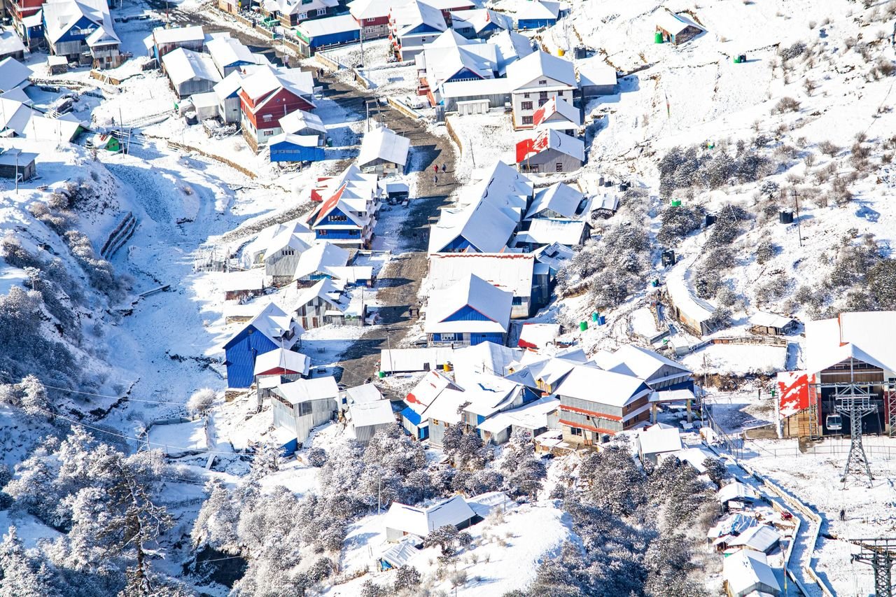 Aerial shot of a snow-covered mountain village with colorful roofs, creating a picturesque winter scene.