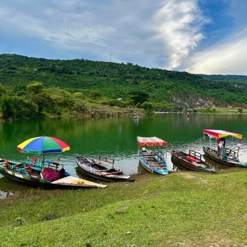 Vibrant wooden boats floating on a serene lake with lush green hills in Meghalaya, India.