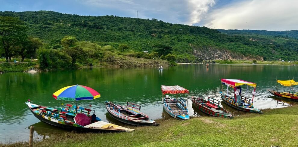 Vibrant wooden boats floating on a serene lake with lush green hills in Meghalaya, India.