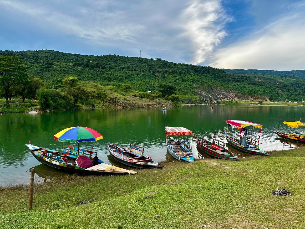Vibrant wooden boats floating on a serene lake with lush green hills in Meghalaya, India.