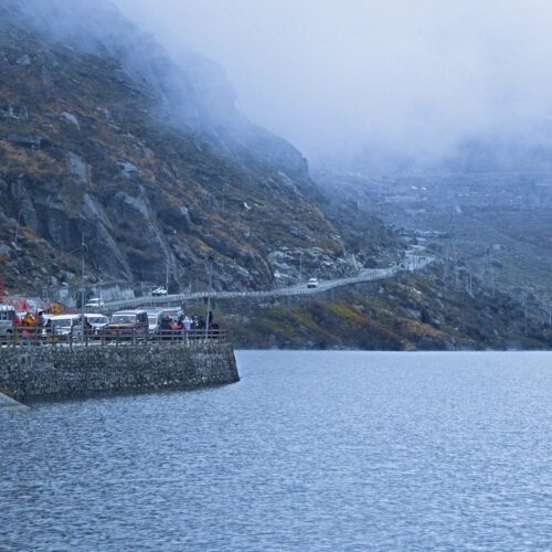 Serene winter scene at a misty lake with mountains and vehicles in Sikkim, India.