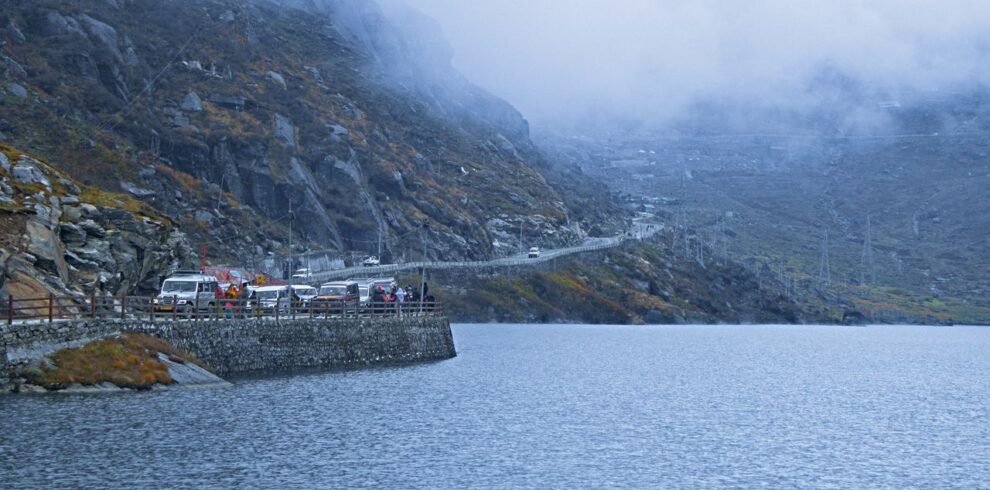 Serene winter scene at a misty lake with mountains and vehicles in Sikkim, India.