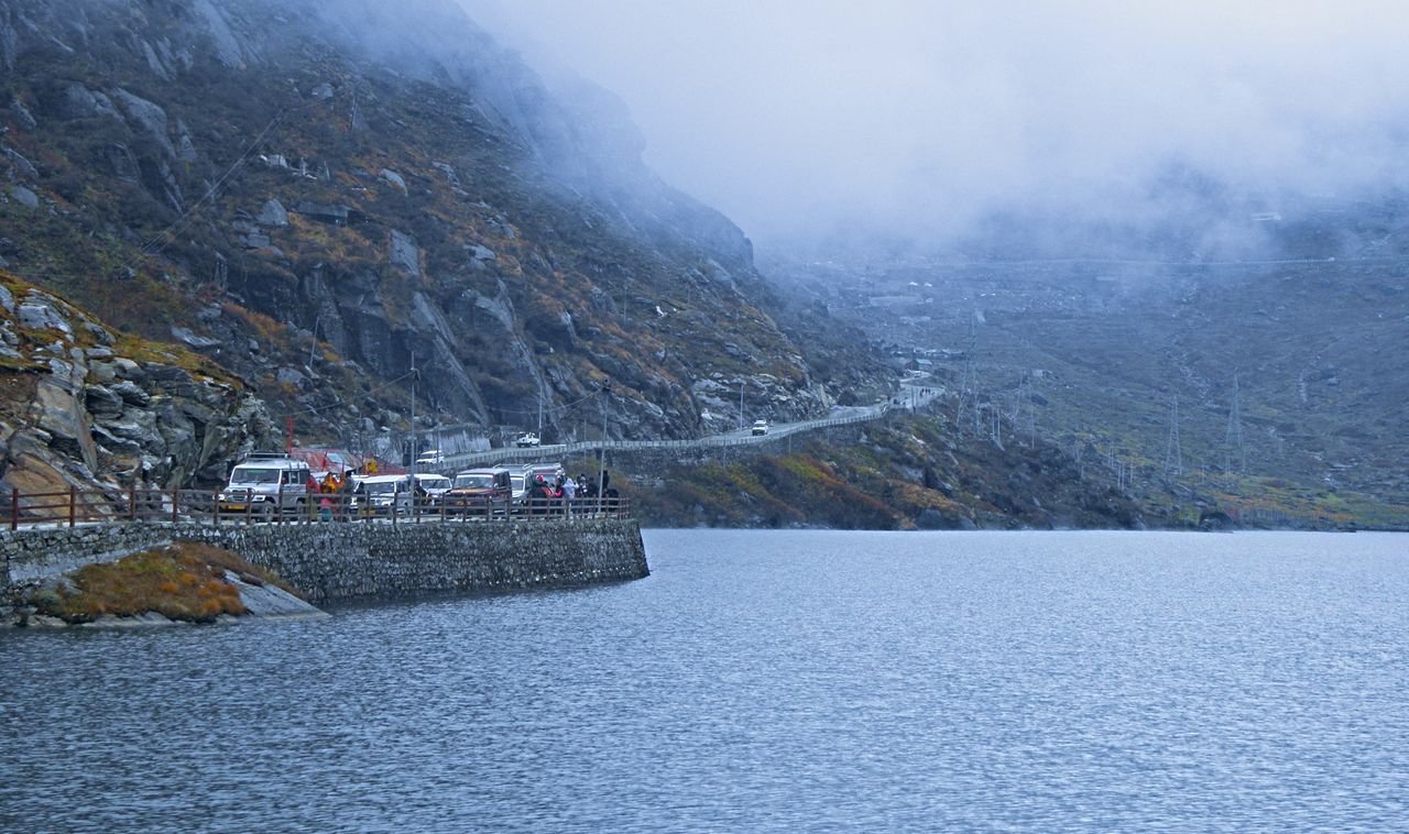 Serene winter scene at a misty lake with mountains and vehicles in Sikkim, India.