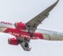 Side view of Air India airplane flying against a clear sky. Captured in detail, showcasing wings and engines.