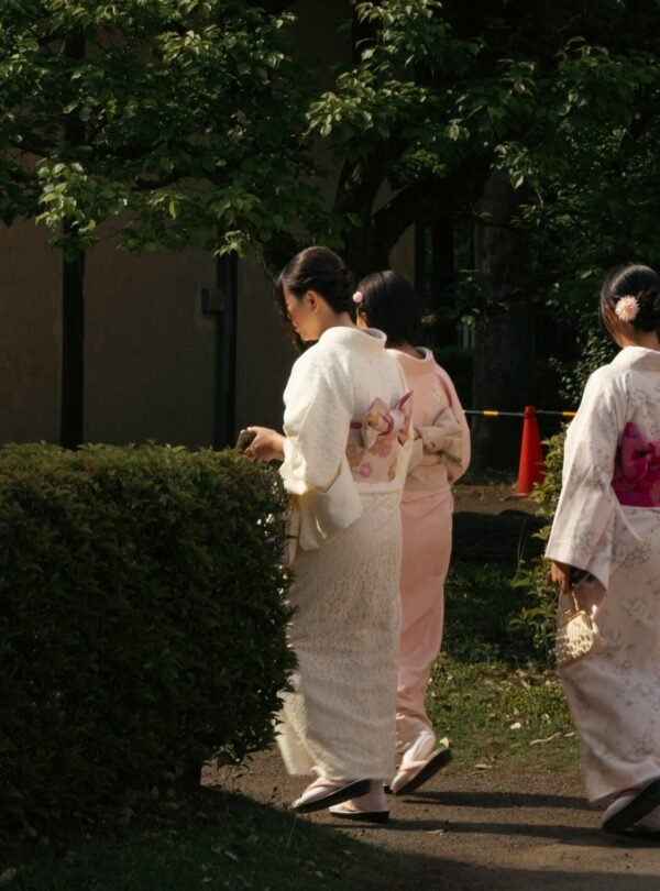 Three women in traditional kimonos strolling in a serene Tokyo garden, capturing cultural elegance.