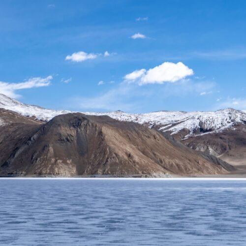 Beautiful snow-capped mountains with a frozen lake under a clear blue sky.